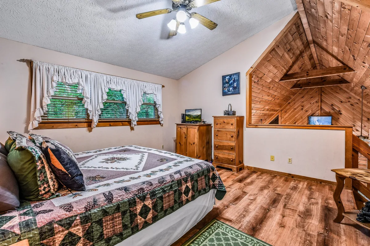 A cozy king bedroom featuring a bed with a quilted cover, wooden furniture, and a window with elegant curtains letting in natural light. The room exudes warmth and comfort, emphasizing plush bedding and a peaceful atmosphere ideal for rest after a day of adventure.