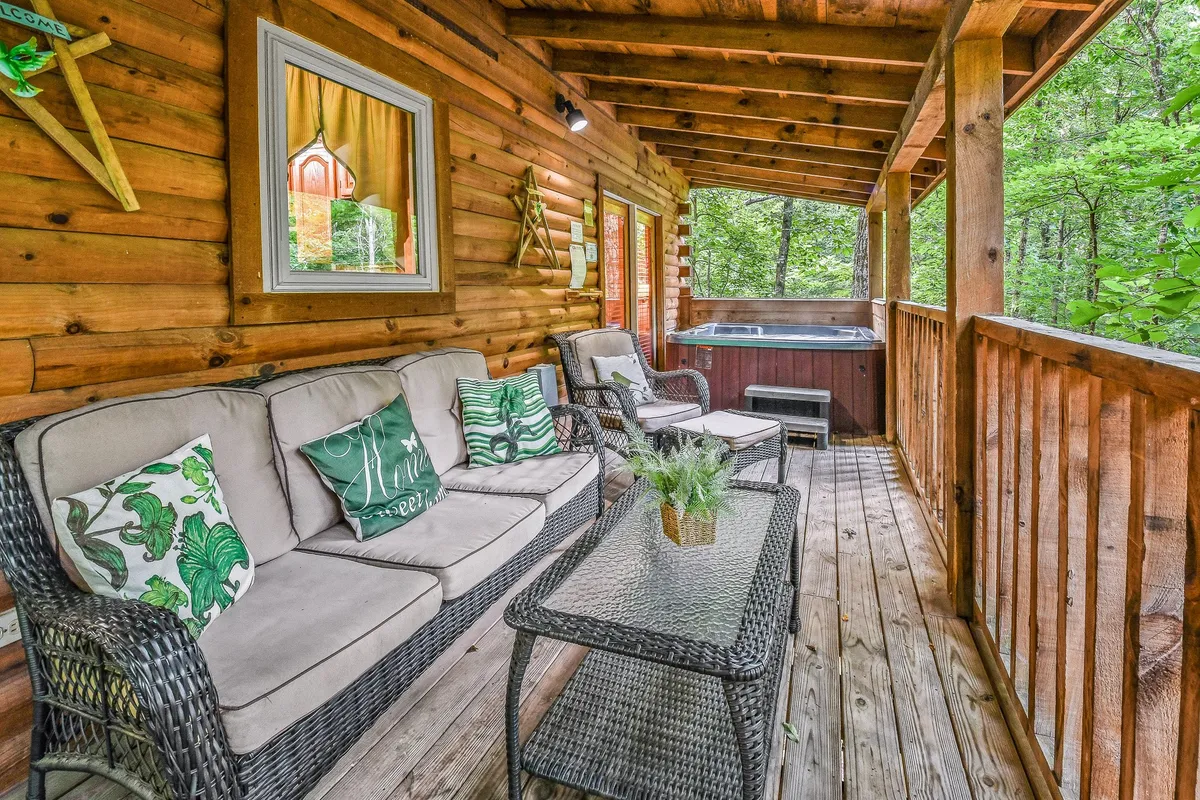 This exterior image features a cozy seating area on a covered porch, accented by a hot tub, plush decorative cushions, and sturdy wooden beams. The ambiance is tranquil, inviting guests to relax together outdoors while soaking in the natural surroundings.