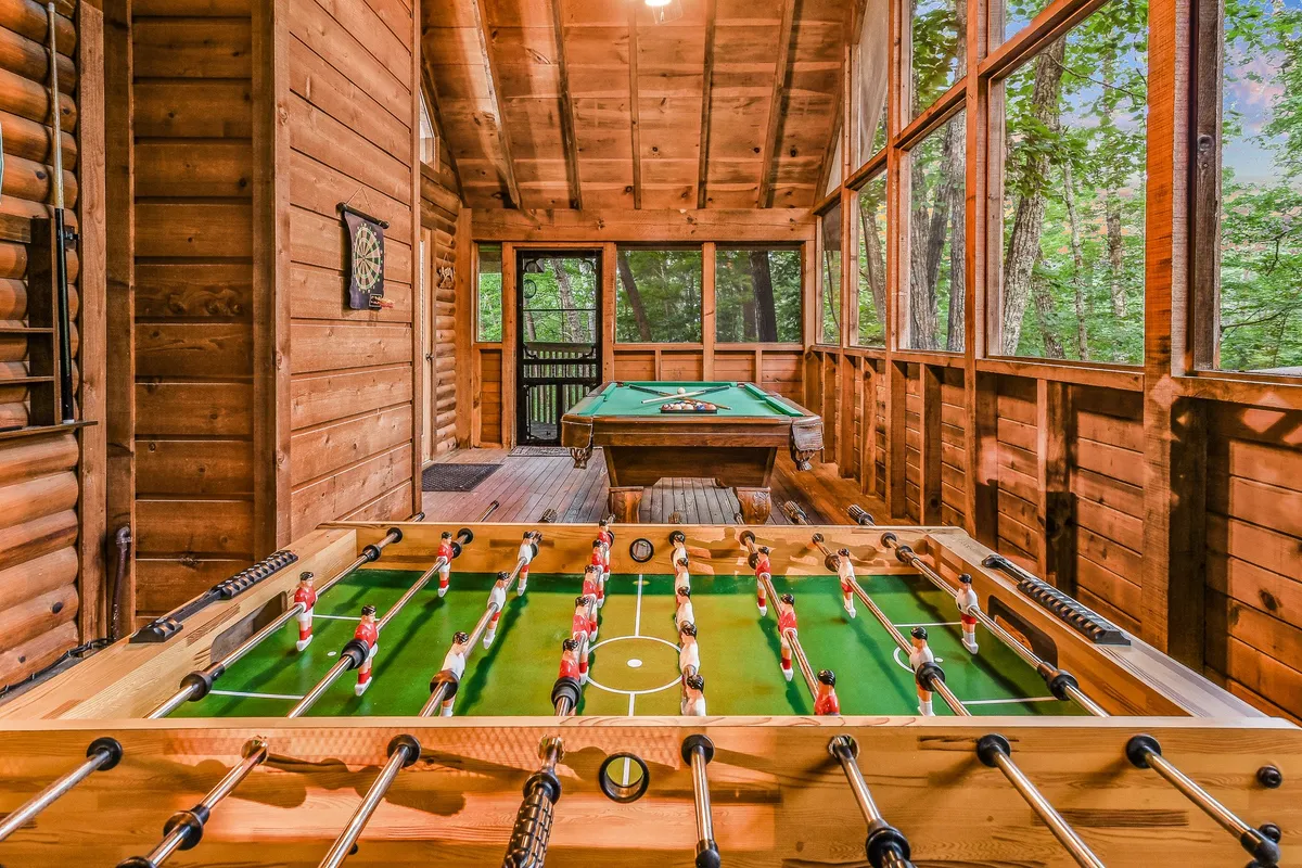 A bright, spacious game area featuring both a foosball and pool table, framed by large windows that let in natural light. The setting is lively and ideal for family game nights and casual hangouts.