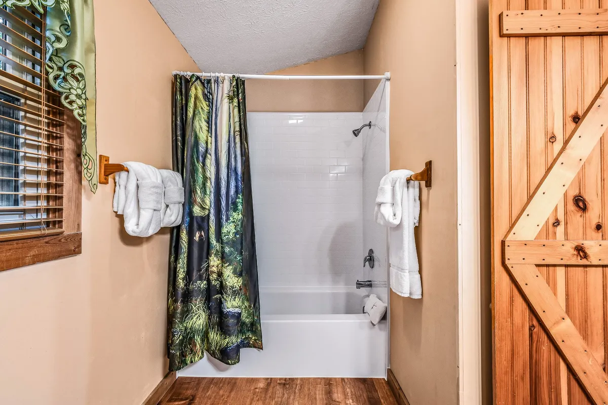 A bathroom with a classic bathtub, shower curtain, and wooden door, evoking a calm and welcoming vibe. The setting suggests a functional yet inviting space suitable for families or friends, matching the description of the upstairs full bath with a shower/tub combo.