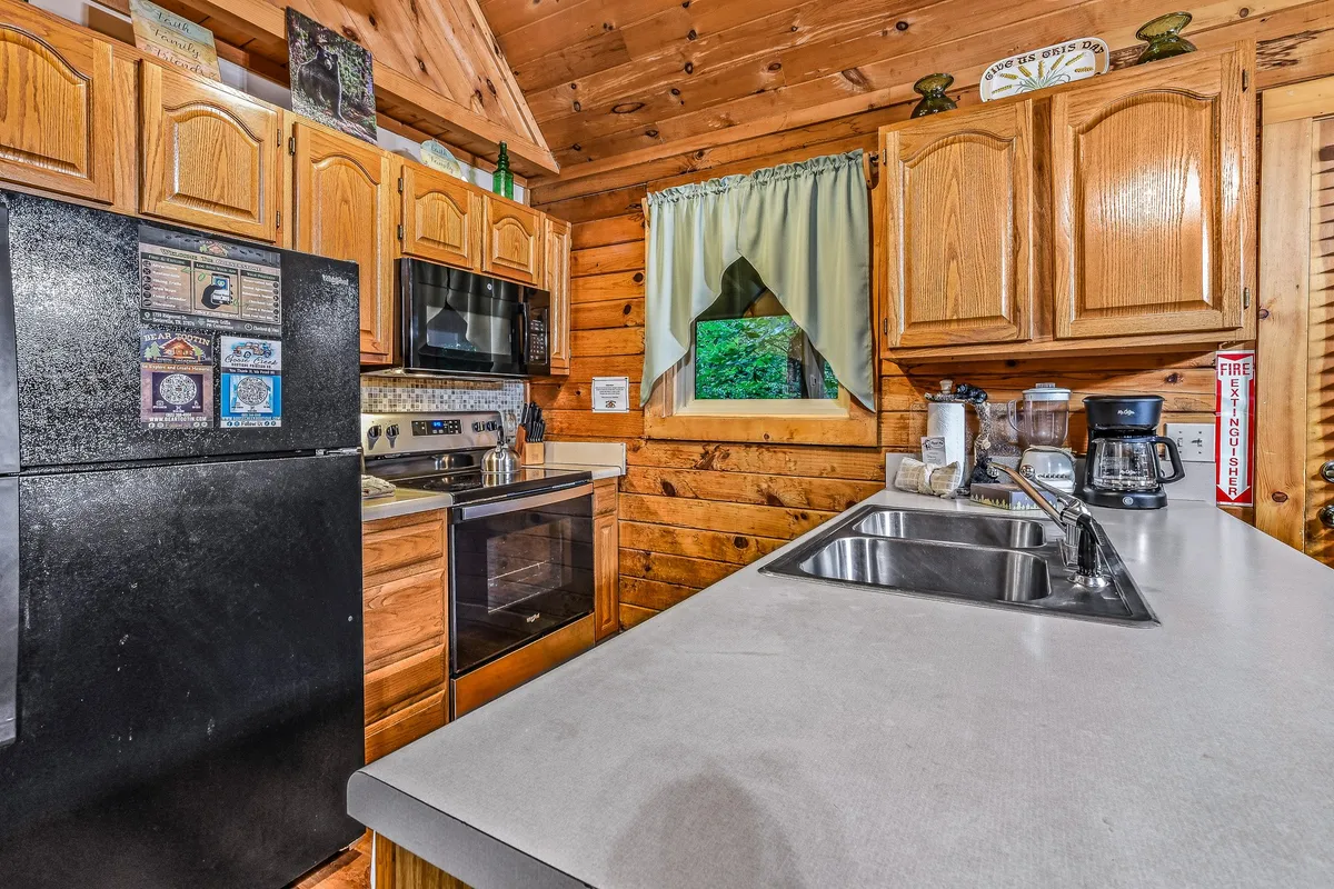 This image showcases a warm, rustic kitchen featuring a spacious countertop, wooden cabinets, a window with green curtains, and modern kitchen appliances. Natural light filters in, highlighting both the functionality and the inviting atmosphere of the space, with ample room for cooking and conversation.