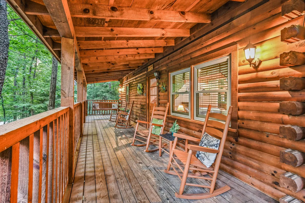 An inviting porch scene with rustic rocking chairs, log walls, decorative plants, and a warm light fixture. The setup encourages quiet moments of reflection, enjoying sunrise views, or stargazing at night, all with a sense of privacy and intimacy.